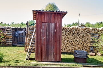 Outdoor toilet in rustic red color on the background of firewood
