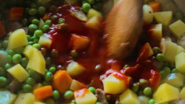 Tomato sauce is added to the dish with peas, potatoes, carrots and meat.
