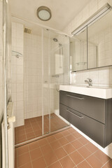 a bathroom with tile flooring and white tiles on the walls, there is a shower stall in the corner