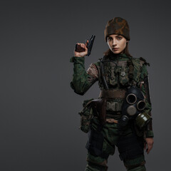 Portrait of a female soldier in military uniform and cap, with a bandaged hand and a pistol, portraying a rebel or partisan in a conflict in the Middle East, against a gray background