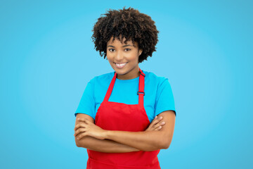 Beautiful laughing african american waitress with red apron on blue background - obrazy, fototapety, plakaty