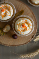 Autumn pumpkin cupcakes with orange sprinkles on top on natural wooden background with real pumpkin behind close up selective focus