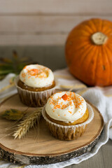 Autumn pumpkin cupcakes with orange sprinkles on top on natural wooden background with real pumpkin behind close up selective focus
