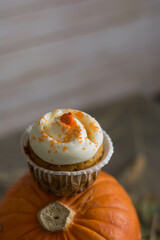 Autumn pumpkin cupcakes with orange sprinkles on top on natural wooden background with real pumpkin behind close up selective focus