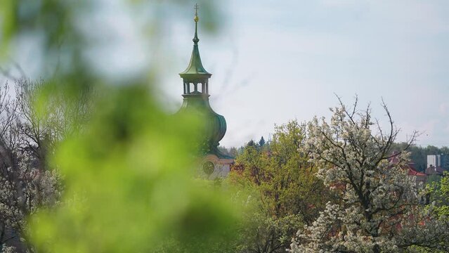 A church spire with a patina-covered roof towers above the blooming spring orchard. Slow-motion parallax shot.
