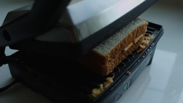 A pice of white bread with butter spread over it is place on top of the marble cheese for the grilled cheese, then the panini press is closed to grill the sandwich.