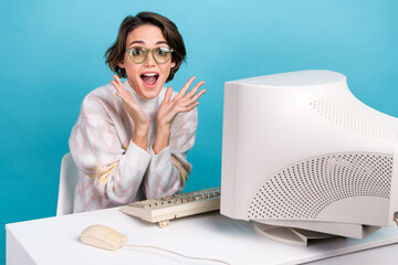Portrait of charming astonished girl open mouth raise hands desktop workplace retro pc monitor isolated on blue color background
