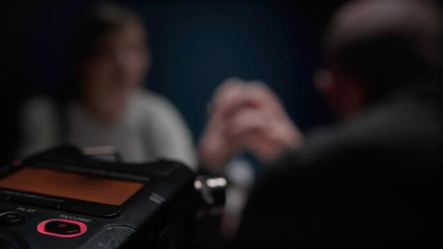 Closeup of digital audio voice recorder, blinking record button. Interrogation by police detective. Suspect denies FBI agent accusations of his guilt. Female officer asks arrested mafia to sign papers