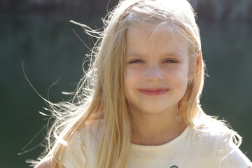 Portrait of adorable little preschool girl with long blonde hair. Idyllic summer day outdoor in nature.