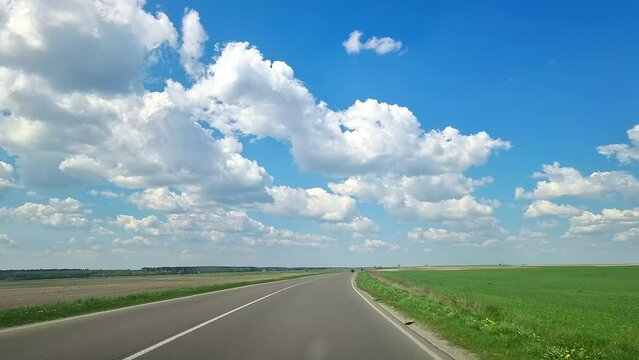 Vehicle point-of-view A view of the road while traveling by car. Green fields and blue sky with clouds. Beautiful nature of the flat landscape.