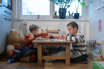 two children draw with crayons. they are sitting at the table. They are getting ready for school.