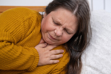 woman 50 years old in yellow sweater holds to heart, sudden chest pain, , Work-Life Balance,...