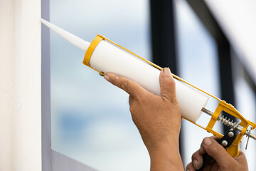 Builders are using a silicone caulking gun to fill a leak between glass and aluminum.