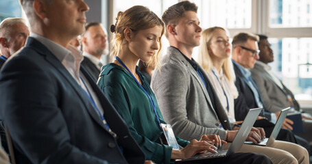 Young Woman Sitting in Crowded Audience at Business Conference. Female Delegate Smiling, Using...