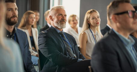 Senior Male CEO Sitting In Crowd At International Technology Conference, Listening To Presentations...