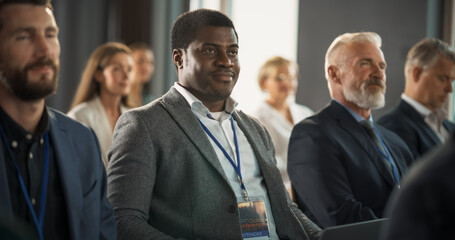 Black Man Sitting in a Crowded Audience at Business Conference. Corporate Delegate Using Laptop Computer While Listening to Inspirational Entrepreneurship Presentation About Developing Markets.