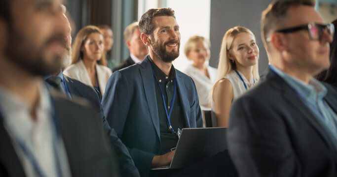 Caucasian Man Sitting in a Crowded Audience at an IT Conference. Delegate Using Laptop Computer to Take Notes. Software Developer Watching Presentation About New High Tech Products and Cloud Solutions