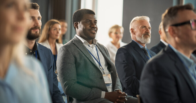 African American Man Sitting in Diverse Crowd At International Business Conference And Listening To Keynote Of Innovative Startup Company. Black Male Investor Attending Global Technology Forum.