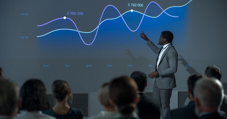 Corporate Event: Black Male Tech CEO Giving Presentation To Colleagues or Investors In Conference Room Of Innovative Startup Office. African Man Talking About Business Objectives, Profit Margins.