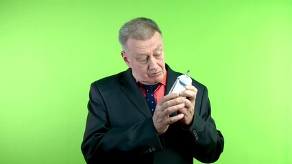 Senior man shakes faulty alarm clock and knocks on it, trying to repair it.