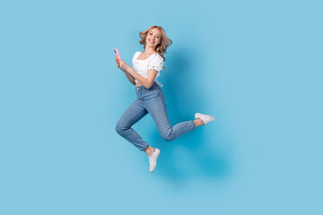 Fototapeta na wymiar Full length photo of pretty cheerful lady wear white blouse jumping high texting modern device isolated blue color background