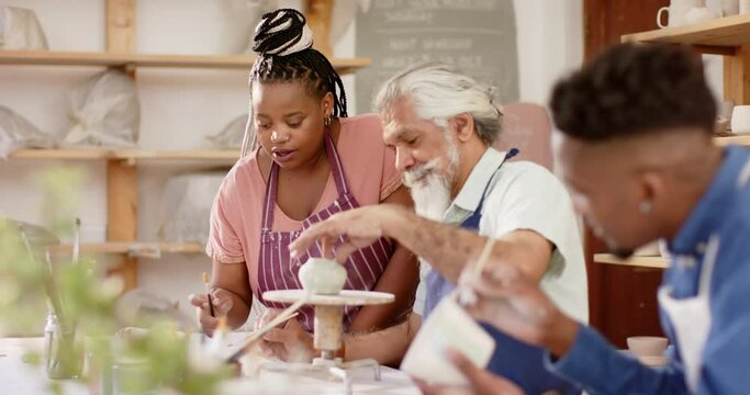 Happy diverse group of potters glazing clay jugs and discussing in pottery studio