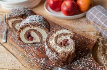 Swiss roll with buttercream and cherries on wooden table