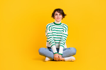 Fototapeta na wymiar Full length photo of young gorgeous woman wear trendy sweater sit floor look empty ad space thinking isolated on yellow color background