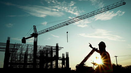 Silhouette of engineer using laptop to control work, crane, construction site - Powered by Adobe