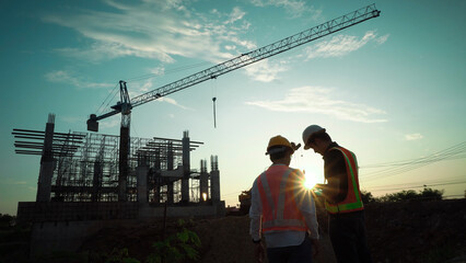 Silhouette of team engineer using laptop to control work, crane, construction site