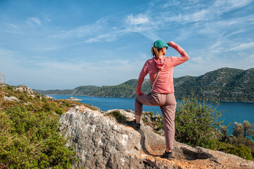 Beautiful traveler woman on mountain peak looking at the sea water in summer. Back pose