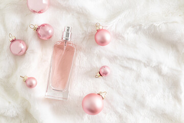 Stylish bottle with cosmetic spray or perfume on fur white background among pink christmas balls. Top view. A copy space. Presentation .