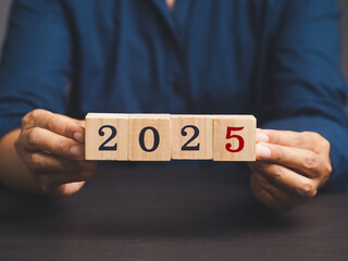 Hand of holding wooden cubes with the number "2025" while sitting at the table.