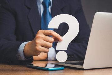 Businessman holds a white question mark symbol sitting at the table.