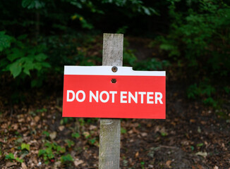 A homemade sign with the inscription “Do not enter” screwed with old screws to a board against the backdrop of dense thickets