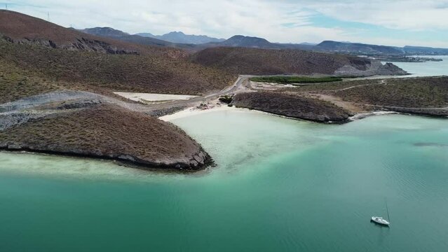 Aerial dolly backwards shot in front of the gorgeous coast of Playa El Tecolote with turquoise sea water, dry summer landscape and pristine beach near Baja California Sur, Mexico during a trip