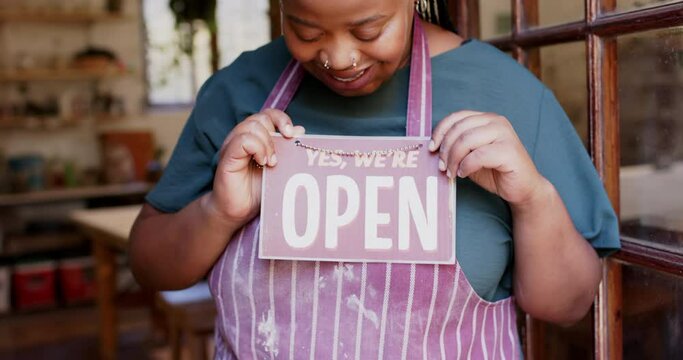 Happy african american female business owner holding shop sign to open and smiling, slow motion