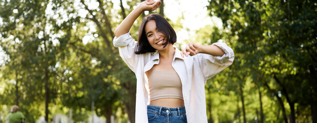 Carefree woman dancing and walking in park with hands lifted up high, smiling happily. Lifestyle concept