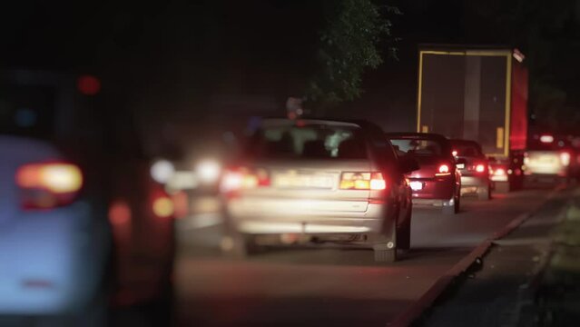 Cars drive and slow down due to traffic jam ahead of road. Rush hour at night out of town. Crowded busy road with stuck vehicles. Cargo truck among passenger automobiles on a two-lane road