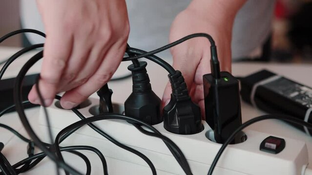 A man unsafely removes live electrical wires and plugs from an electrical surge protector. Cotsnept safety violation, short circuit and electric shock, close-up. Slow motion