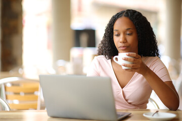 Black woman drinking coffee using laptop in a bar
