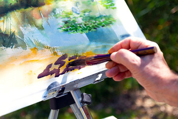 close-up detail of the watercolour painter painting a watercolour painting with a brush on an easel.