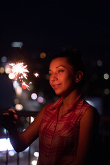 Beautiful young woman portrait holding a sparkler in the city at night 