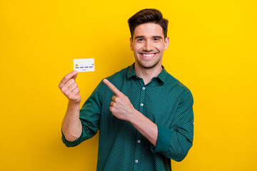 Photo of positive nice man wear trendy green clothes arm demonstrate plastic card nfc payment isolated on yellow color background