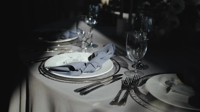 Close-up wedding table decoration: served plates, glasses on the table, sun light rays on the plate, blue napkin on the table. Festive table decor, all decorated in pastel blue colors, slow motion. 