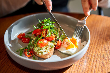 Open brioche sandwich with mint avocado, poached egg served with arugula and cherry tomato. Healthy breakfast. Toast with guacamole, vegetable and poached egg and eggs benedict with brioche