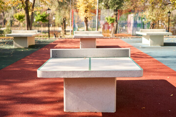 Table tennis tables in autumn public park. Concrete tennis table in a city park ping pong game - obrazy, fototapety, plakaty