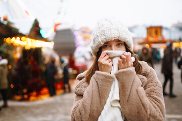 Young woman in winter style clothes posing at festive street market. Woman enjoying winter moments....