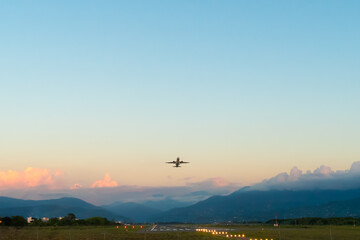 White passenger plane takes off against a beautiful sky with golden clouds and green mountains....