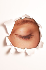 woman eye closed, behind a hole in a white paper